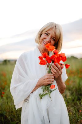 Claudine Vergaert souriante dans un champ de coquelicots tenant un bouquet de coquelicots dans se mains
