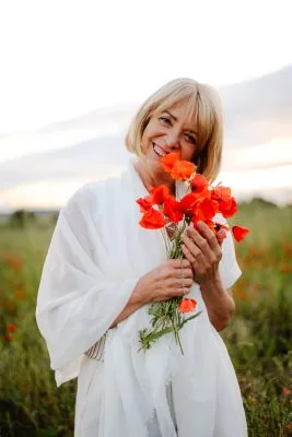 Claudine Vergaert souriante dans un champ de coquelicots tenant un bouquet de coquelicots dans se mains